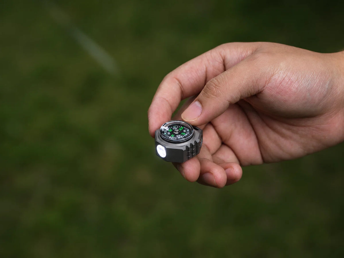 FIELDLUME T9 titanium EDC torch held in hand with built-in compass and white light on